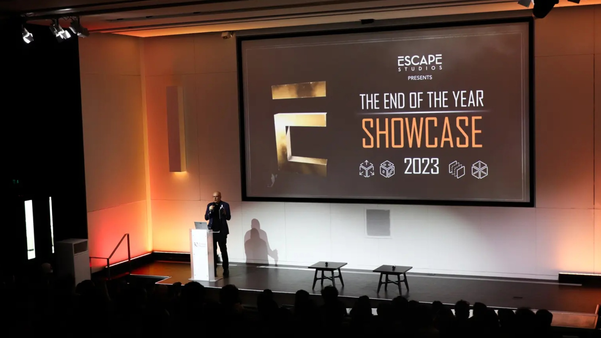 Principal of Escape Studios on a stage in front of a screen that reads The End of The Year Showcase 2023