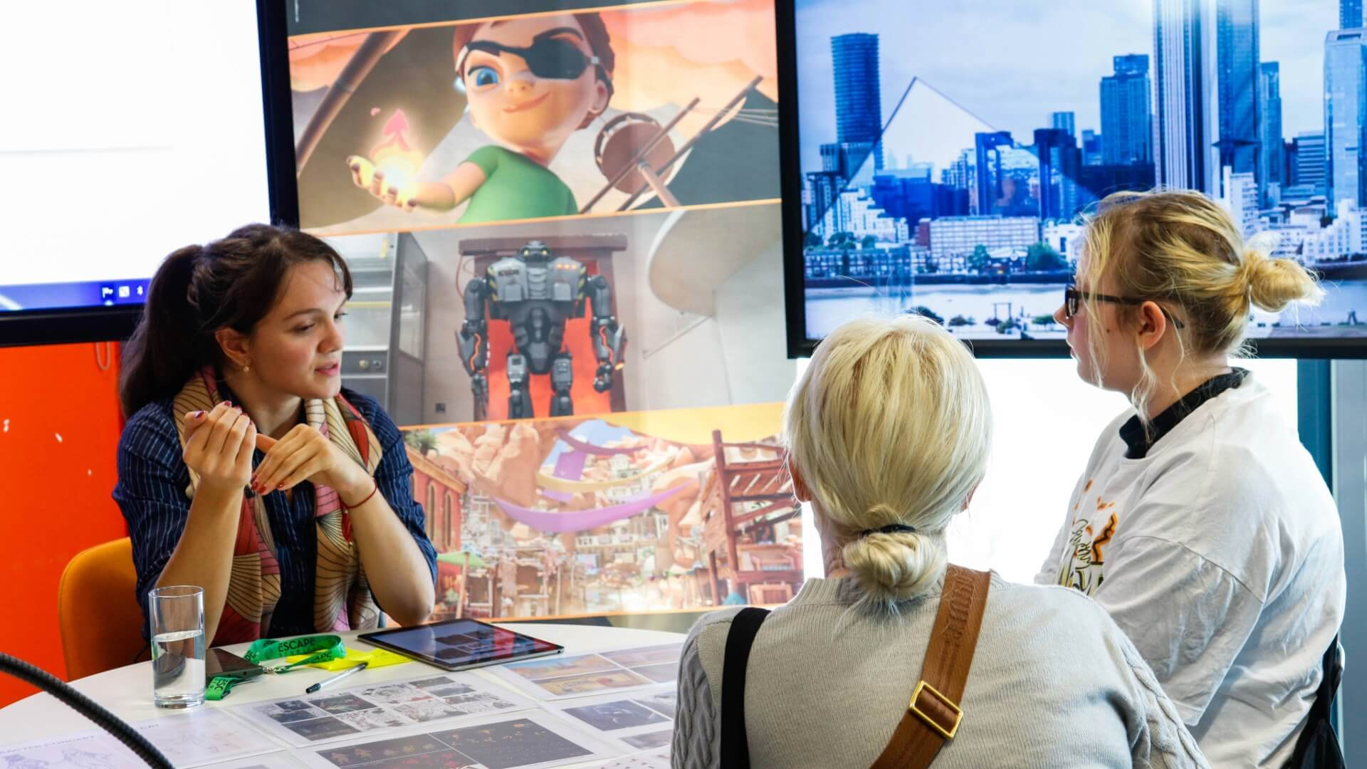 Three people discuss animation design, surrounded by sketches and screens displaying animated characters and cityscapes.