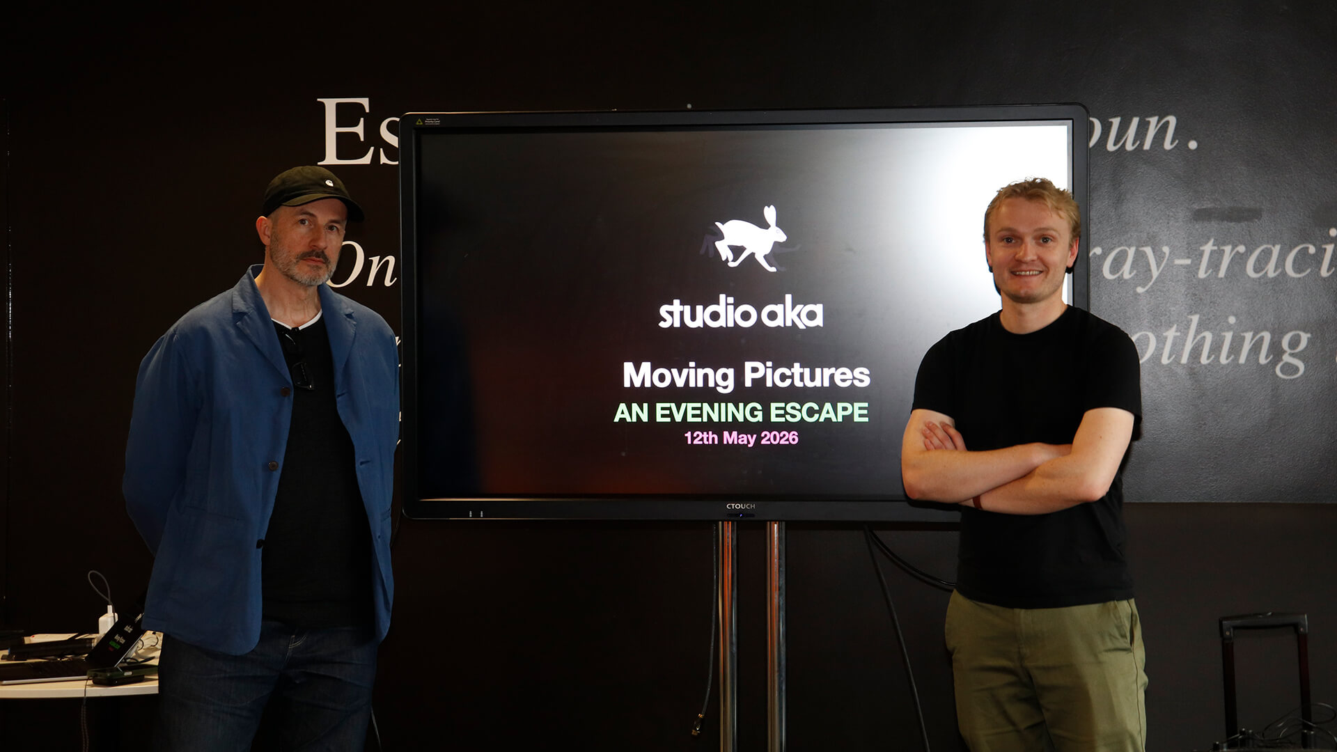 Two representatives from Studio AKA standing in front of a screen which reads: Studio AKA. Moving pictures. An Evening Escape. 12th May 2026.