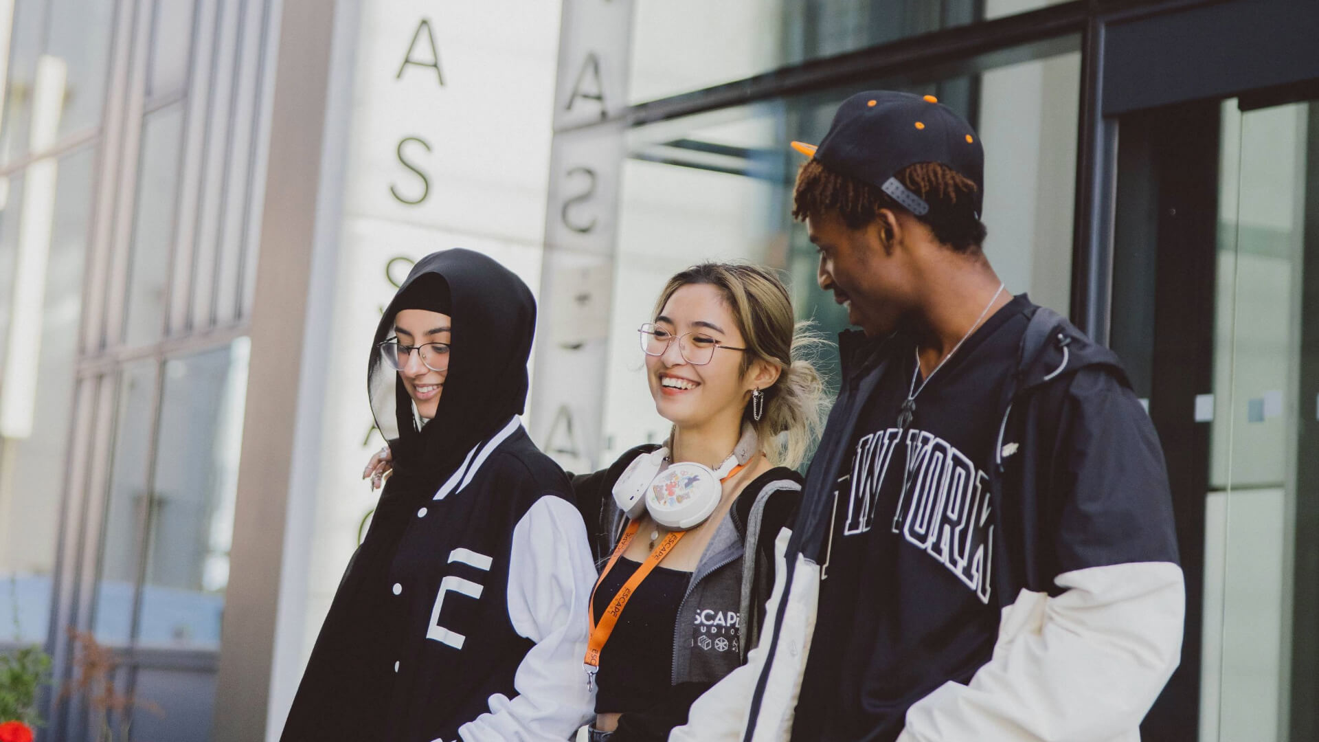 Three Students wearing Escape jackets and lanyards talking and walking away from a building entrance