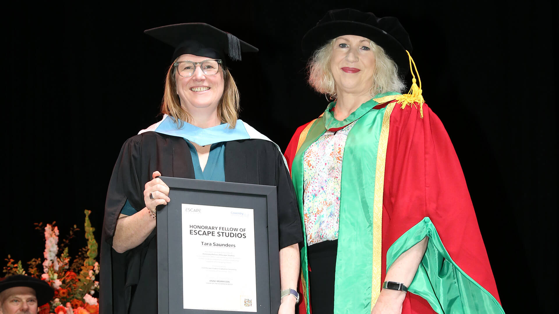 Tara Saunders stood with Anne Morrison at the Escape Studios Graduation. Tara is holding her honorary fellowship certificate.