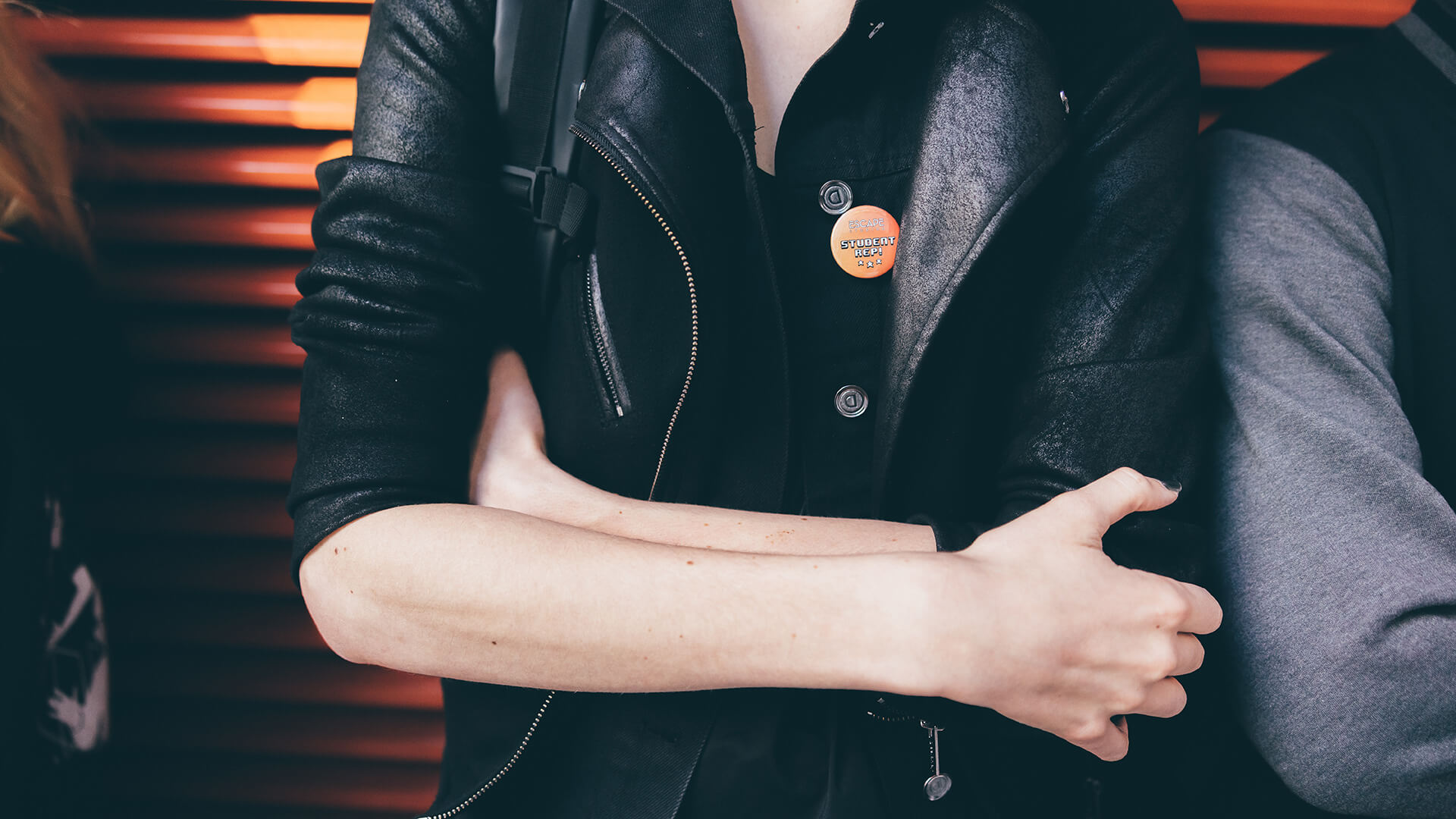 Student with arms crossed in front of orange wall