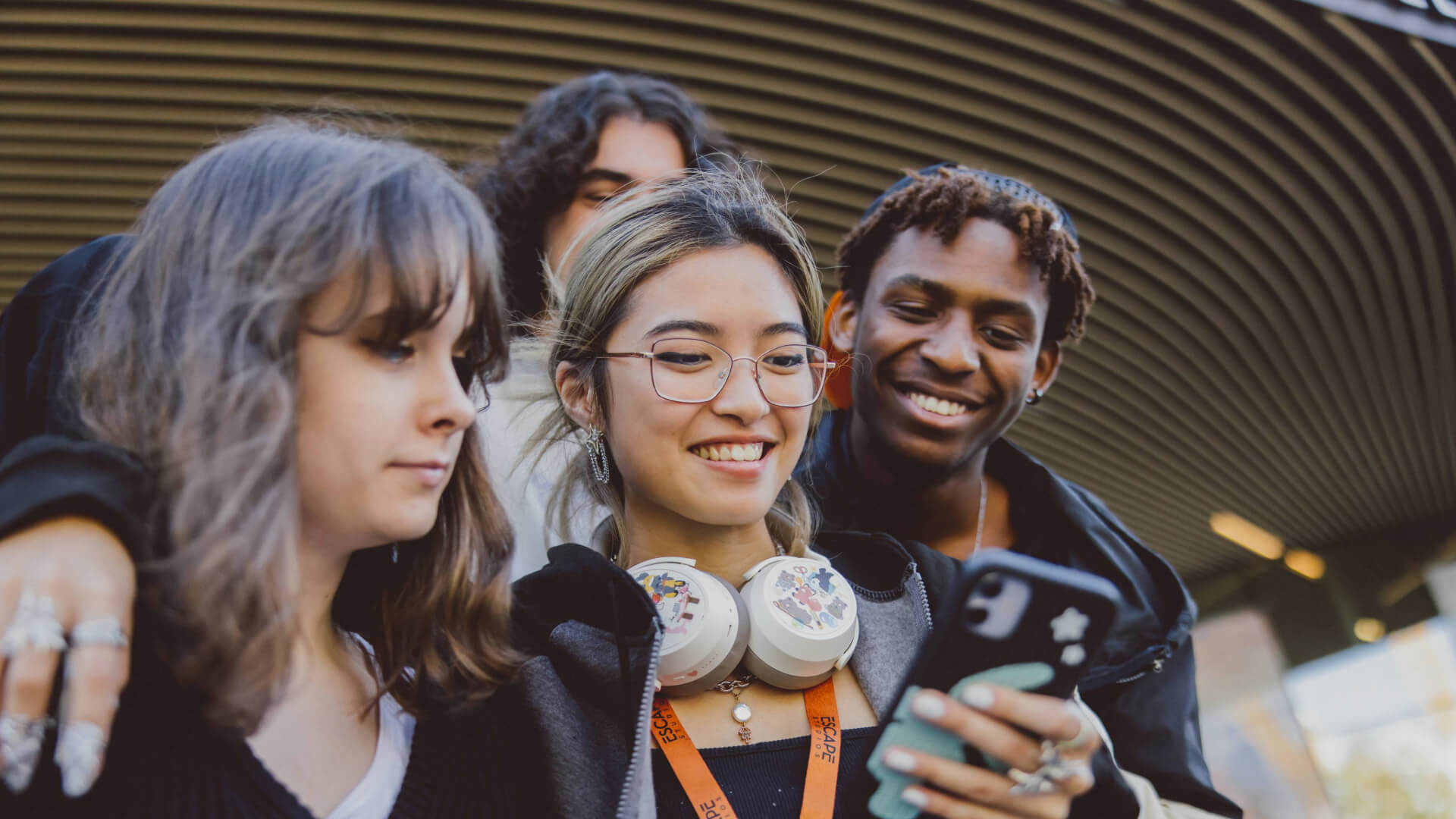 Four students outside looking at a phone and smiling.