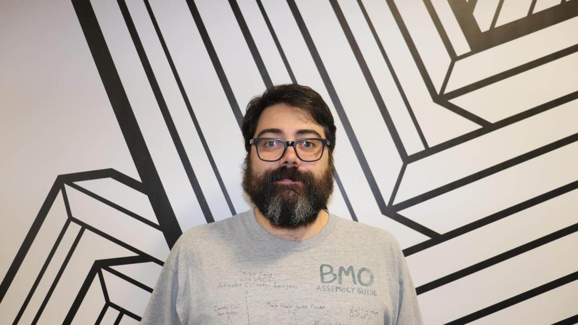 Headshot of James Valades Marquez stood in front of a black and white stripey wall