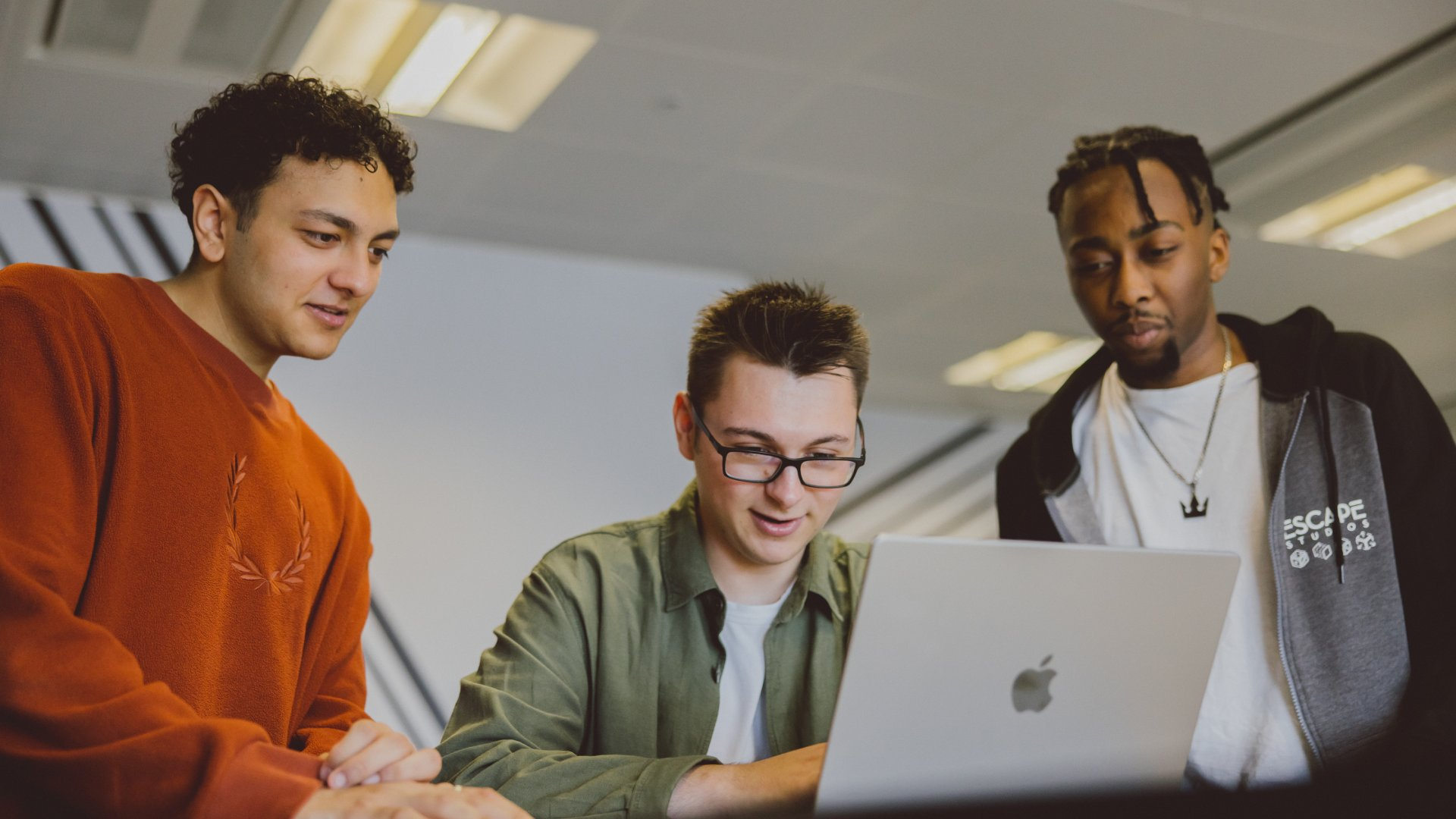 Three students working on one laptop in the Escape studios campus
