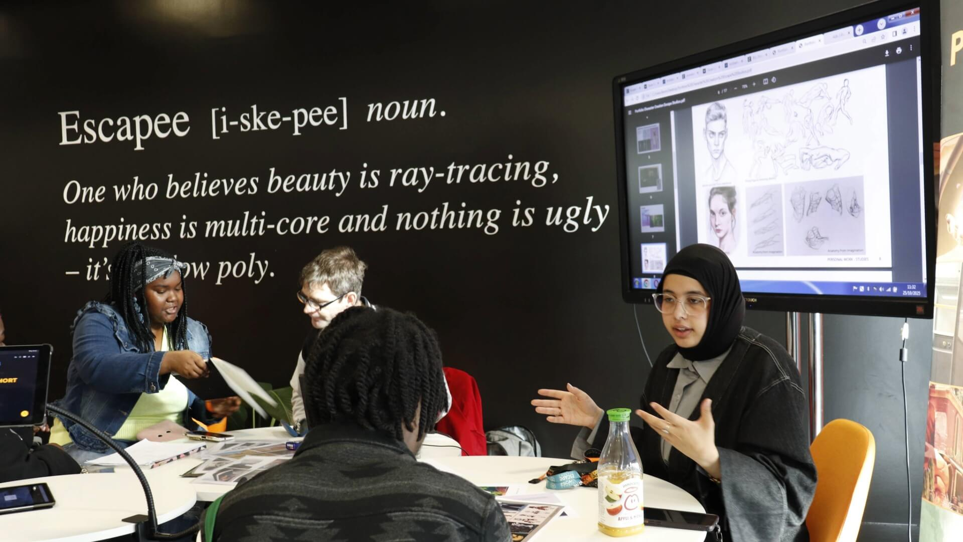 an Escape Studios Tutor and Studio Assistant speak to open day guests at the Portfolio Station table