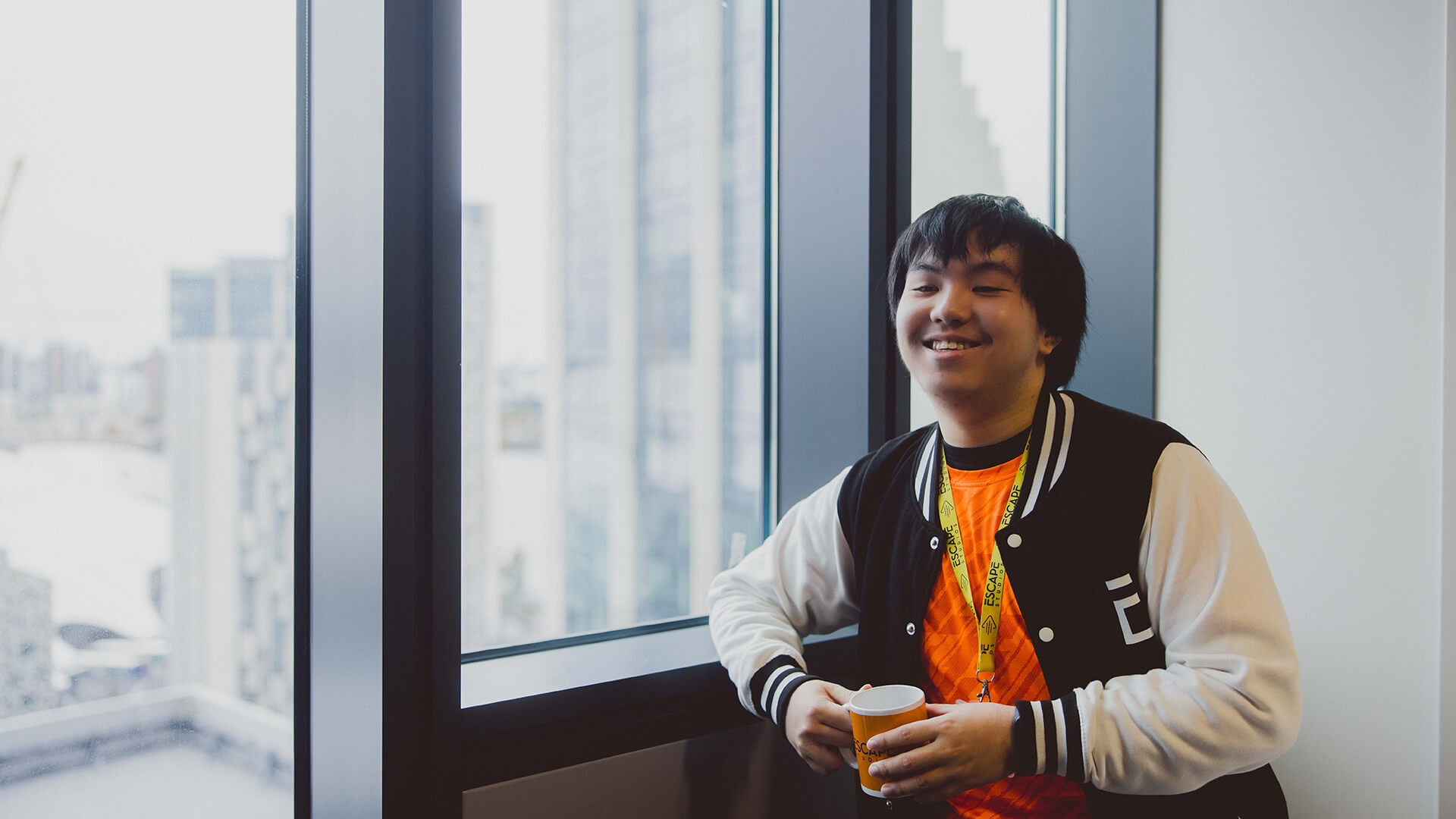 Student stood by the window in the campus kitchen holding a coffee mug and smiling