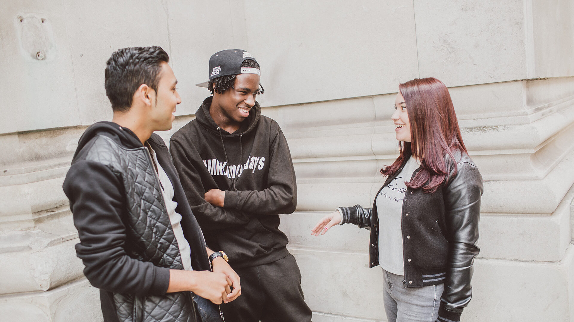 Three students chatting against stone wall