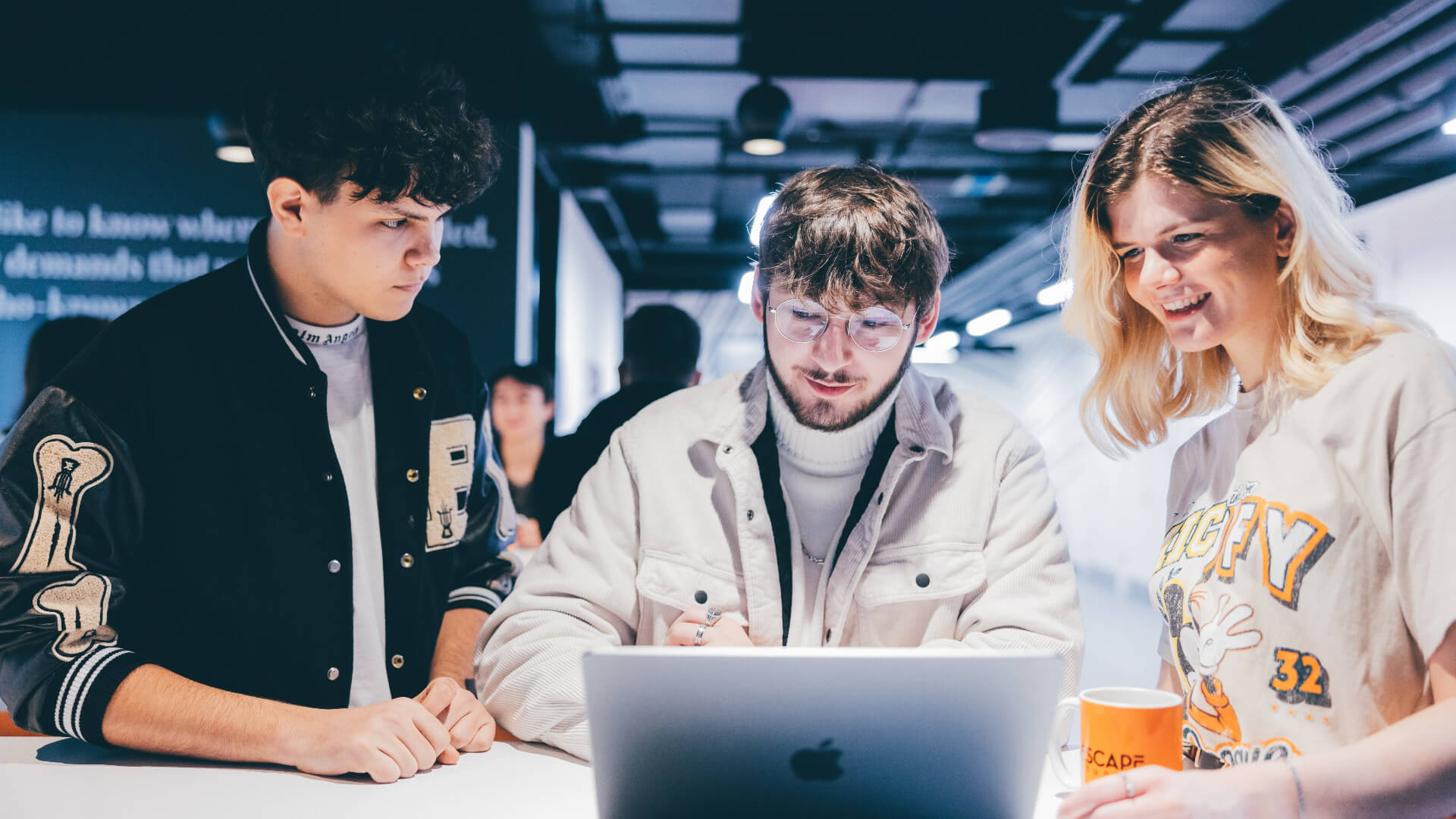 Three students are gathered around a laptop in one of the Escape Studios campus breakout spaces